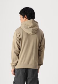 Huva i beige fleece med avslappnad passform, med en stor huva och ribbade muddar. Sparas med mörka cargobyxor.