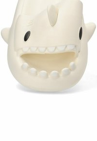 Chancla de goma blanca diseñada para parecerse a la cabeza de un tiburón, con una boca sonriente con dientes afilados, ojos negros redondos y aletas pequeñas.