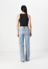 Black sleeveless top paired with light blue high-waisted straight-leg jeans. Jeans feature back pockets and a contrasting tan leather patch.