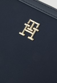 Portafoglio in tessuto texturizzato blu navy con un prominente logo monogramma dorato, con finitura liscia e linee pulite.