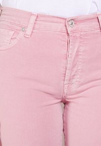 Jeans in denim rosa chiaro con un design aderente, dotati di un bottone argentato e cuciture a contrasto in vita e sulle tasche.