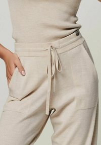 Beige gestrickte Jogginghosen mit elastischem Bund, Kordelzug und seitlichen Taschen. Glatte Textur und lockere Passform.