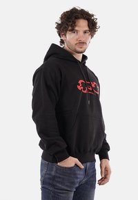 Felpa nera con un design grafico rosso sul davanti, dotata di tasca a canguro e cappuccio regolabile con cordino. Tessuto morbido.