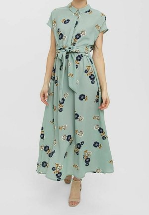 Blommig maxiklänning i ljusgrön tyg med korta ärmar, knäppning med knappar, midjeband och spridda mörkblå och vita blommönster.