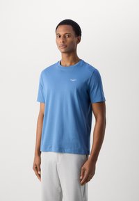 Blauwe T-shirt met korte mouwen, gemaakt van zachte stof, met een ronde hals en een klein logo op de borst. Eenvoudig, veelzijdig ontwerp.