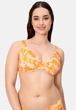 Mujer con un top de bikini de patrón floral en tonos naranja y crema, sonriendo, con cabello largo y oscuro sobre un fondo claro y liso.