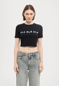 Mustat lyhythihaiset cropped-t-paidat, joissa on valkoiset "BLA BLA BLA"-tekstit leikkisässä fontissa. Yhdistetty vaaleansinisiin korkeavyötäröisiin farkkuihin.