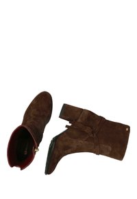 Botas de tobillo de ante marrón con un forro rojo, detalles atados en el eje y un tacón grueso. Presentan una puntera redonda y una suela texturizada.