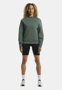 Tumeroheline kapuutsiga sweatshirt, kitsas lõikega, soonikute ja hemiga. Koos mustade rattapükstega. Tekstuurne kangas, millel on logo detail rinnal.