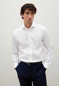Witte langemouwen shirt met een standaard kraag, met een knoopsluiting aan de voorkant en een gladde textuur, gedragen met marineblauwe geblokte broek en een zwarte leren riem.