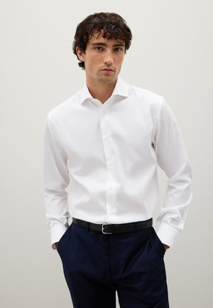Weißes Langarmhemd mit Standardkragen, ausgestattet mit einer Knopfleiste und glatter Textur, getragen mit navyfarbener gemusterter Hose und schwarzem Leder Gürtel.