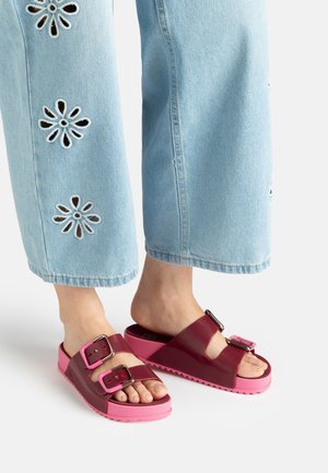 Person wearing light blue jeans with flower cutouts and pink slide sandals with two dark pink buckled straps.