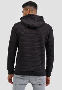 Donker gestructureerde hoodie met een verhoogd patroon, voorzien van een capuchon, ribgebreide manchetten en zoom. Draagt met lichtgekleurde jeans voor contrast.
