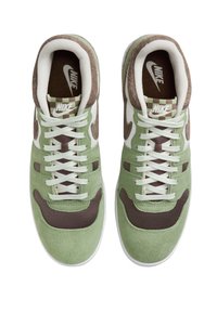 Pár zelených, hnědých a bílých tenisek Nike s bílými tkaničkami, kostkovaným detaily na jazyku a logem Nike na vnitřních solech a jazycích.