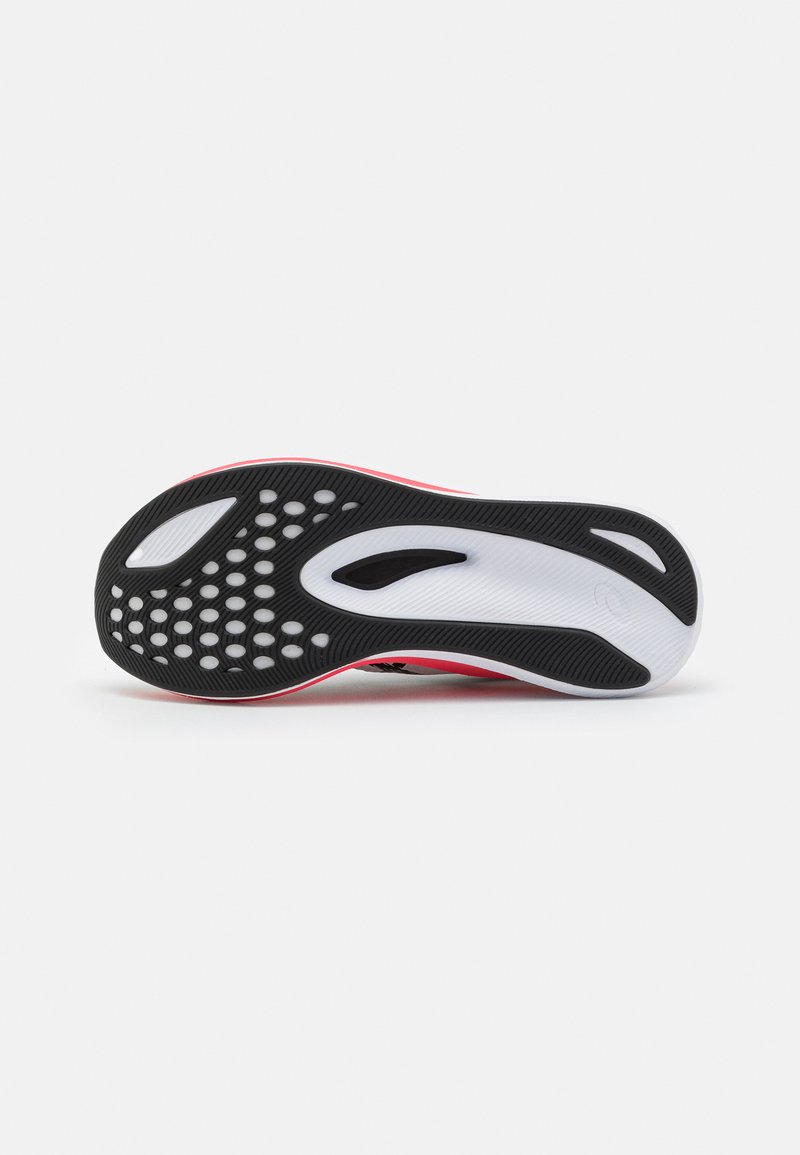 Semelle de chaussure de sport noire et rose avec un caoutchouc noir texturé, une semelle intermédiaire blanche et des motifs de grip circulaires pour une meilleure adhérence.