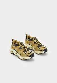 Zapatos deportivos Gore-Tex en tonos marrón y negro, con un upper texturizado, sistema de cordones y suela gruesa blanca. Presentan tiradores en los talones.
