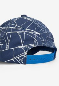 Marineblaues Cap mit weißen abstrakten Linien, ausgestattet mit einem verstellbaren Kunststoffriemen und einem strukturierten Stoff. Offenes Rückendesign für Atmungsaktivität.