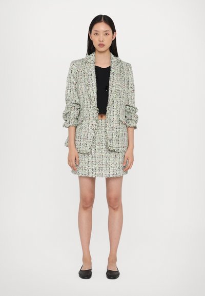 Tweed-Blazer- und Rock-Set in Pastellfarben, strukturiertes Gewebe, puffige Ärmel des Blazers, kombiniert mit einem schwarzen Crop-Top und schwarzen Ballerinas.
