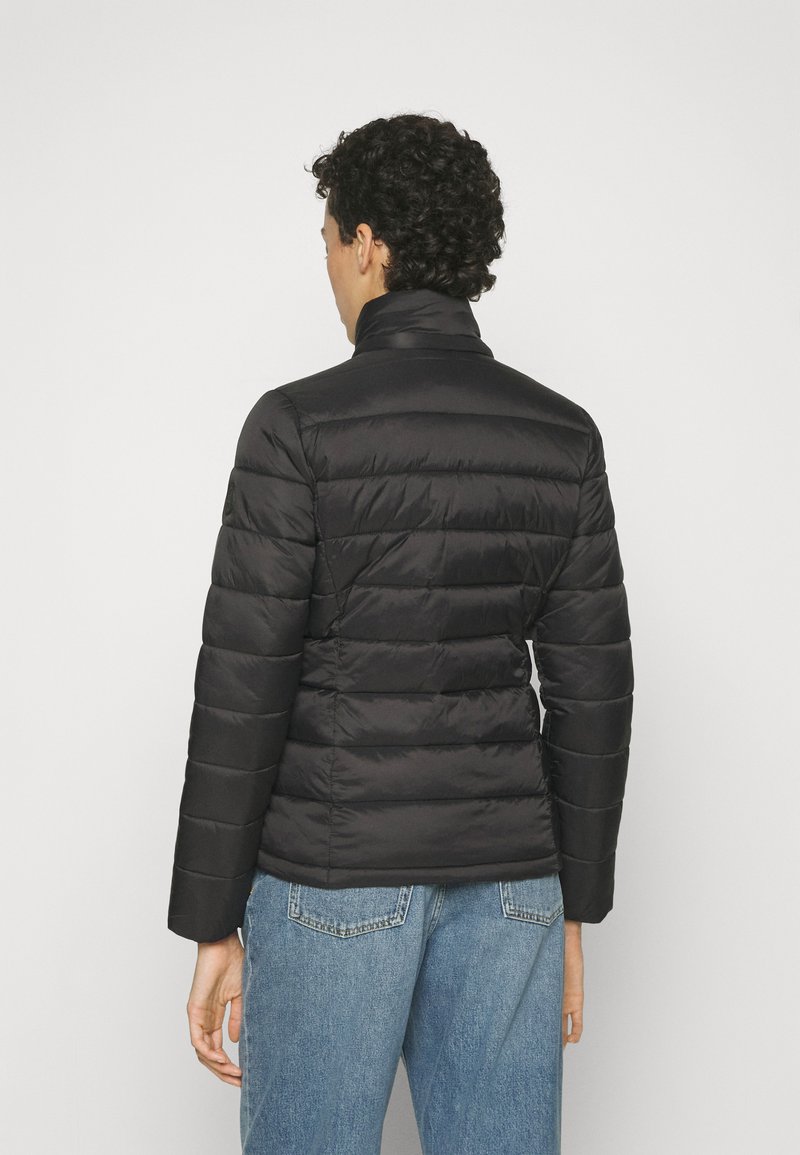 Chaqueta de plumas negra con cuello alto, diseño acolchado y superficie texturizada. Combinada con jeans de cintura alta en un tono azul claro.