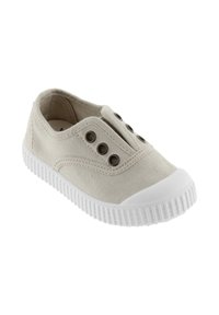 Beige canvas slip-on sneakers med hvid gummisål og tåhætte, med fire metaløjer på hver side uden snørebånd.