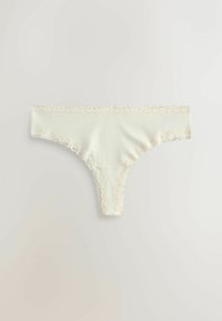 Kvinders trusse i cremefarve med delikat blondekant ved talje og benåbninger, lagt fladt på en hvid overflade.