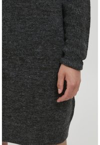 Abito a collo rotondo grigio scuro lavorato a maglia con finitura testurizzata. Maniche lunghe con polsini e orlo a coste. Una mano visibile di lato.