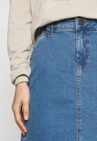 Džínová sukně světle modré barvy se rovný střih, předním zapínáním na knoflíky, kapsami a jemným zesvětlením pro texturu.