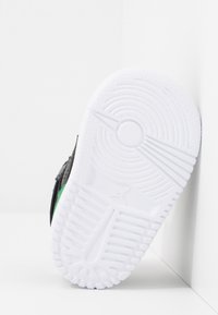 Bílá podešev tenisky s kruhovým vzorem a malým logem Jumpman, natočená proti bílé rohové zdi.