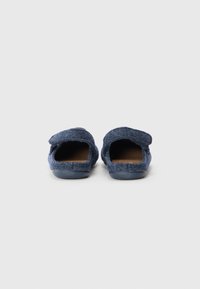 Mörkblåa tofflor i textil med öppen baksida, platt sula och enkel sömdetalj längs kragen.