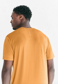 Krótki rękaw, okrągły dekolt koszulki sportowej w ciepłym pomarańczowym kolorze, wykonanej z oddychającej tkaniny o fakturowanej powierzchni i odblaskowymi detalami.