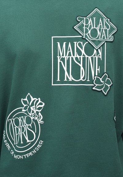 Πράσινο ύφασμα με λευκό κείμενο και γραφικά λουλουδιών που περιλαμβάνουν τις λέξεις "MAISON KITSUNÉ," "PALAIS ROYAL" και "TOKYO PARIS GALERIE DE MONTPENSIER."