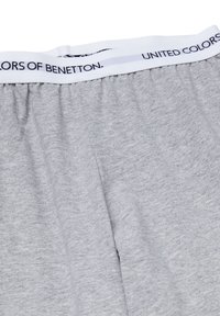 Světle šedá bavlněná látka s elastickým bílým lemem v pase, na kterém je černý nápis "United Colors of Benetton" obepínající lem.