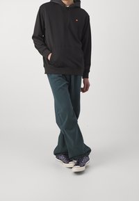 Felpa nera con zip e tasca a marsupio, abbinata a pantaloni verde scuro a vestibilità rilassata e sneakers con motivo. Design semplice, stile casual.