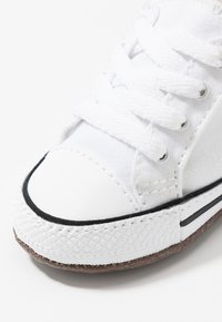Baskets en toile blanches avec un bout arrondi, une bande en caoutchouc noire et une semelle texturée. Elles disposent de lacets blancs et d'œillets en métal.