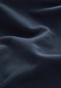 Dunkelblauer Baumwollstoff mit glatter Textur, der sanfte Falten und subtile Lichtvariationen auf der Oberfläche zeigt.