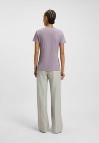 Lila lyhythihainen t-paita, joka on valmistettu pehmeästä kankaasta, yhdistettynä vaaleanharmaisiin leveälahkeisiin housuihin, joissa on yksinkertainen muotoilu ja suora leikkaus.