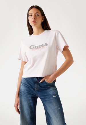 Maglietta in cotone rosa chiaro con logo "Guess" in argento metallico e testo "Nineteen Eighty One", con maniche corte e vestibilità rilassata.