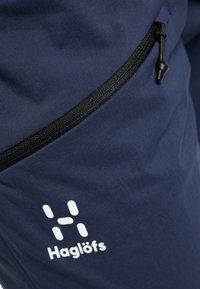 Navyblauwe outdoorbroek met een zwarte rits en een wit Haglöfs-logo. De stof is glad met een lichte glans en een duurzame textuur.
