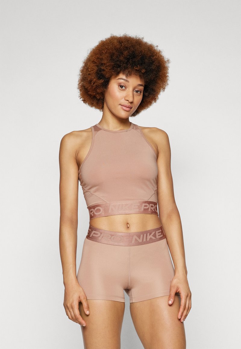 Set di reggiseno sportivo e pantaloni corti color marrone chiaro realizzati in tessuto elasticizzato. Il reggiseno sportivo presenta un elastico con "NIKE PRO" in una tonalità abbinata.