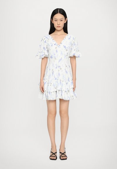 Rochie cu imprimeu floral, cu decolteu în V, mâneci scurte cu volane și tiv stratificat. Prezintă flori albastre deschise pe un fundal alb.