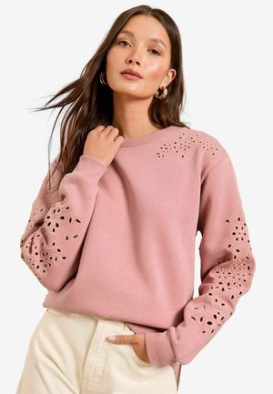 Felpa rosa con motivi floreali ritagliati decorativi sulle maniche. Presenta un colletto girocollo a coste e una texture di tessuto morbido.