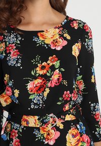 Robe florale en tissu noir avec des roses colorées et de petites fleurs. Encolure ronde, manches longues et une ceinture avec une boucle en argent.