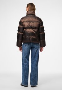 Brun vadderad jacka med hög krage, med en blank yta och quiltad design. Kombinerad med ljusblå vida jeans.