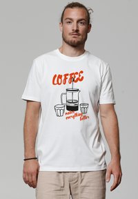 Weißes Baumwoll-T-Shirt mit einem Grafikmotiv eines Kaffeekochers und zwei Tassen, mit dem Text „KAFFEE macht alles besser“ in Orange.