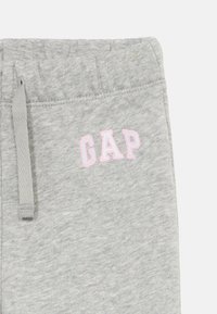 Ljusgrå sweatpants med elastisk midja, dragsko och rosa broderad "GAP"-logga på vänster sida nära framfickan.