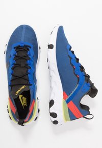 Nike löparskor med en blå tygöverdel med svarta accenter, en vit sula och livfulla röda och gula detaljer.