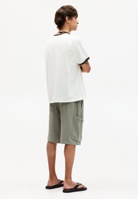 Hvid bomulds t-shirt med brun kant, parret med grønne teksturerede shorts med sidelommer. Bæret med sorte flip-flops.