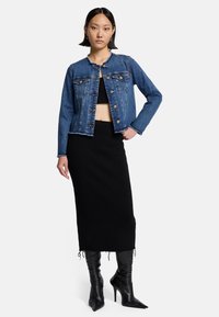 Denimjacke mit einem kurzen Schnitt, hellblauer Farbe, Knöpfen vorne, zwei Brusttaschen, kombiniert mit einem schwarzen Strickrock und spitzen schwarzen Stiefeln.