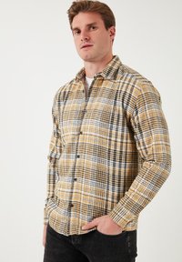 Geel en zwart geruit flanellen shirt met een knoopsluiting aan de voorkant, lange mouwen en een ruime pasvorm. Kenmerkt zich door contrasterende witte lijnen overal.