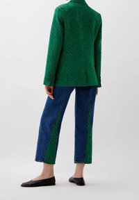 Blazer verde con un diseño de rayas de tigre, combinado con pantalones de mezclilla azul que tienen paneles laterales verdes y zapatillas negras.